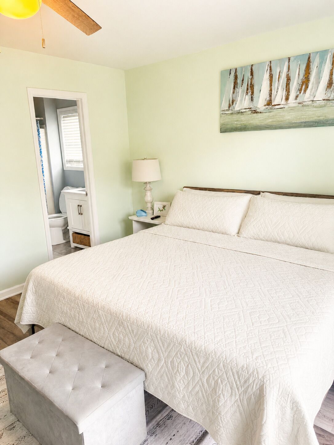 A bedroom with a large bed, a bench, a nightstand with a lamp, a painting on the wall, and a closet with a window.