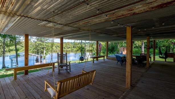 A wooden deck with a swing, chairs, and a view of a lake.