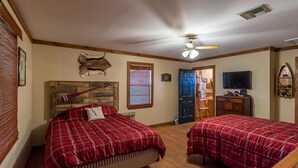 A room with two beds, a ceiling fan, a mounted television, and a door leading to another room.