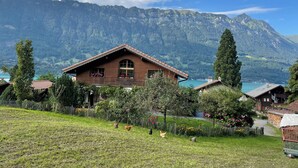A wooden chalet with a sloped roof, surrounded by a lush garden and a mountain backdrop. - Chalet W/Studio in Bönigen by Interlaken on Lake Brienz  (Bönigen by Interlaken)