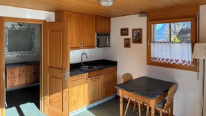 A kitchen with wooden cabinets, a sink, and a window with a view of trees. - Chalet W/Studio in Bönigen by Interlaken on Lake Brienz  (Bönigen by Interlaken)