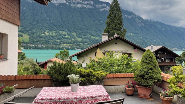 A terrace with a table, potted plants, and a view of a lake and mountains. - Chalet W/Studio in Bönigen by Interlaken on Lake Brienz  (Bönigen by Interlaken)