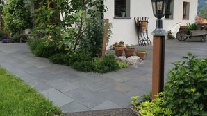 A courtyard with a paved walkway, potted plants, a wooden bench, and a lamp post. - Chalet W/Studio in Bönigen by Interlaken on Lake Brienz  (Bönigen by Interlaken)