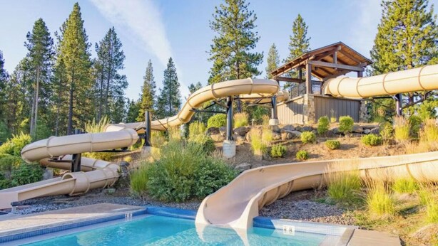 A pool with multiple slides, a wooden deck, and a building with a roof. - Beautiful 4 Bedroom Renovated Home with A/C; 10 SHARC Passes (Sunriver)