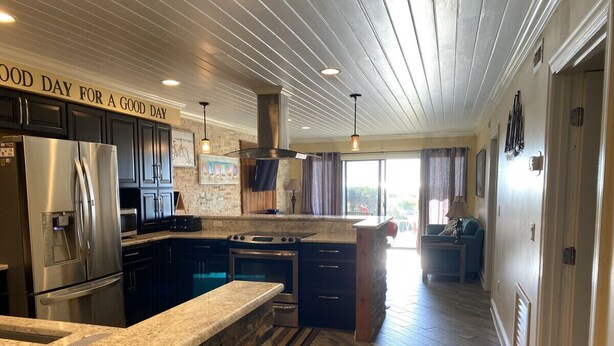 A modern kitchen with granite countertops, stainless steel appliances, and a stone backsplash. - 405 Captain John Fripp Villa - Ocean Front - Ground Level (Fripp Island)
