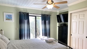 A bedroom with a bed, a ceiling fan, a TV, and a door. - 405 Captain John Fripp Villa - Ocean Front - Ground Level (Fripp Island)