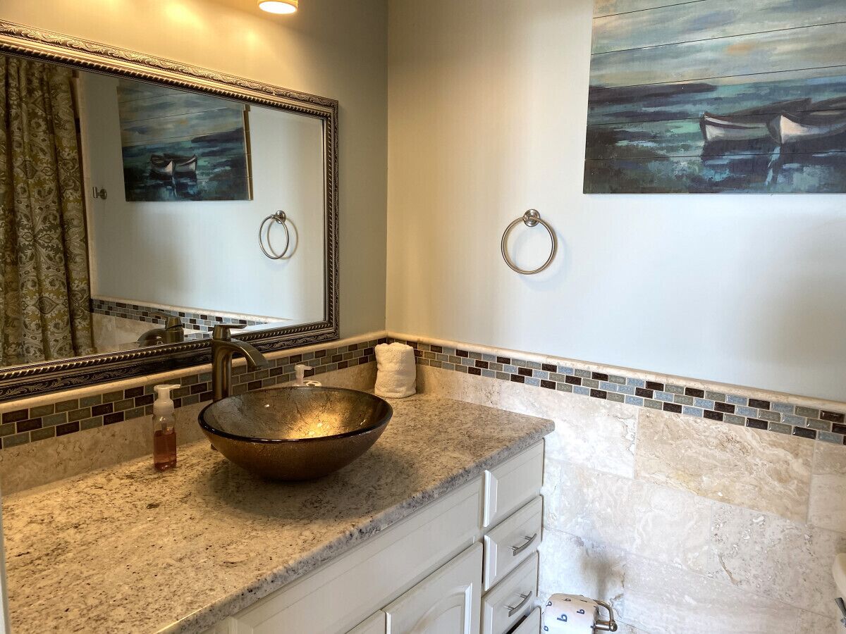Une salle de bain dotée d’un grand miroir, d’un lavabo rond, d’un porte-serviettes et d’une bordure décorative en mosaïque.