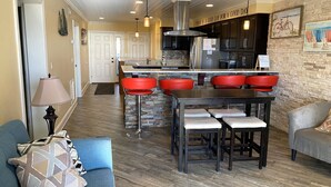 A modern kitchen with a central island, red bar stools, and a dining table. - 405 Captain John Fripp Villa - Ocean Front - Ground Level (Fripp Island)