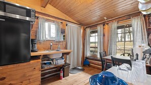 Et interiør af en træhytte med tekøkken, spiseplads og store vinduer.