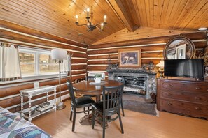 A log cabin interior with a dining table, chairs, a fireplace, a television, and a mirror.