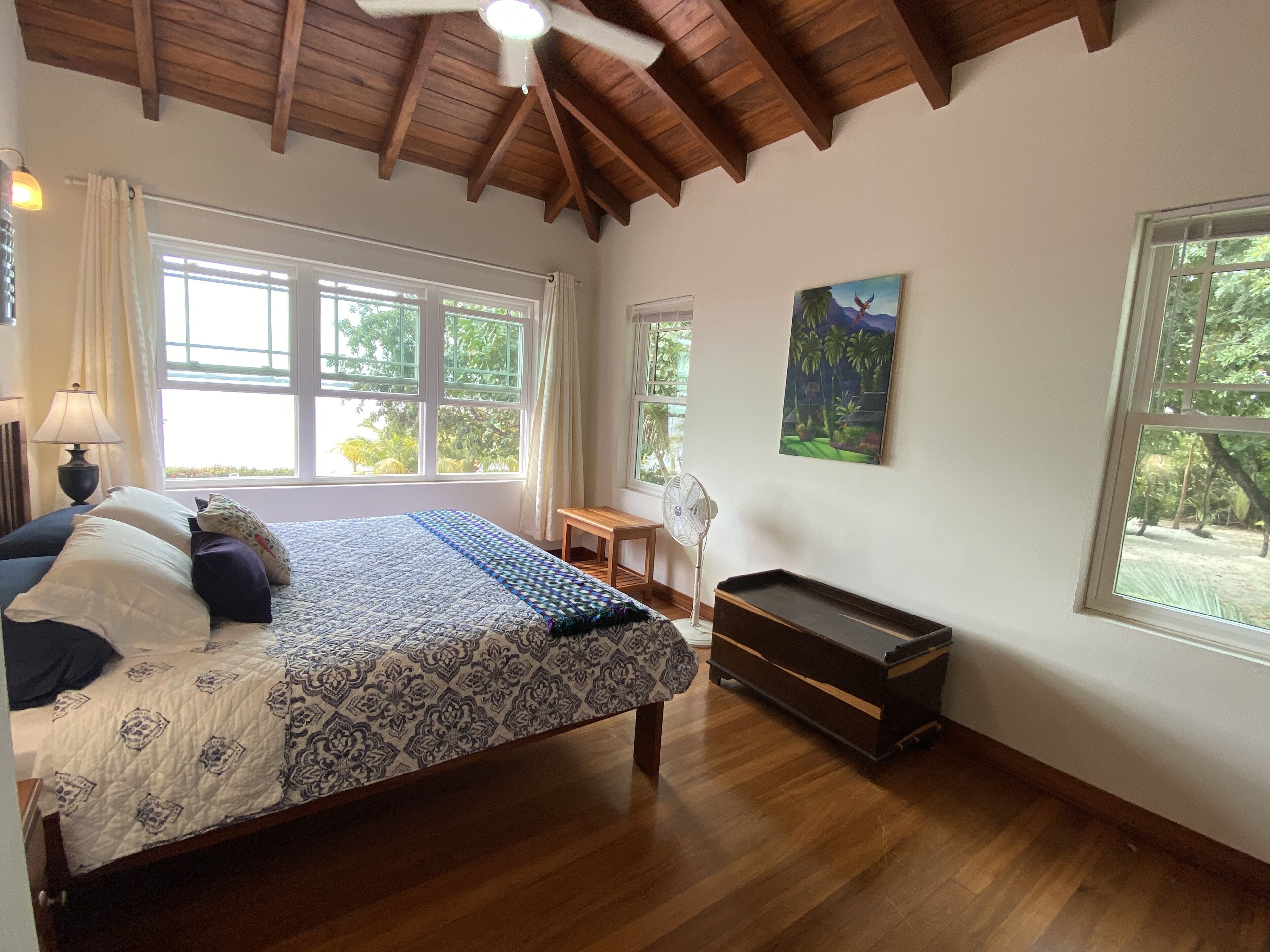 A bedroom with a bed, a desk, a fan, and a piano.