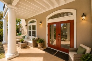 A covered porch with a seating area, a wooden door, and wall-mounted lights.