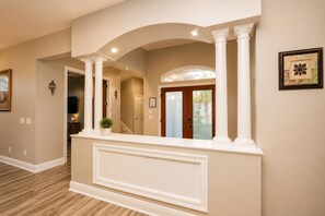 A reception area with a white reception desk, white columns, a framed artwork, and a door leading to another room.