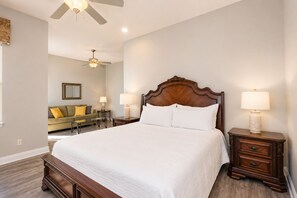 A bedroom with a large bed, two bedside tables with lamps, a ceiling fan, a green sofa, and a small table with a lamp.