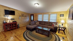 A cozy living room with a sectional sofa, a coffee table, and a television on the wall.
