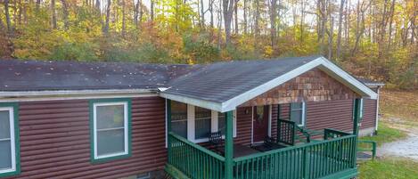 A cabin with a porch and a small deck, surrounded by trees with autumn foliage.