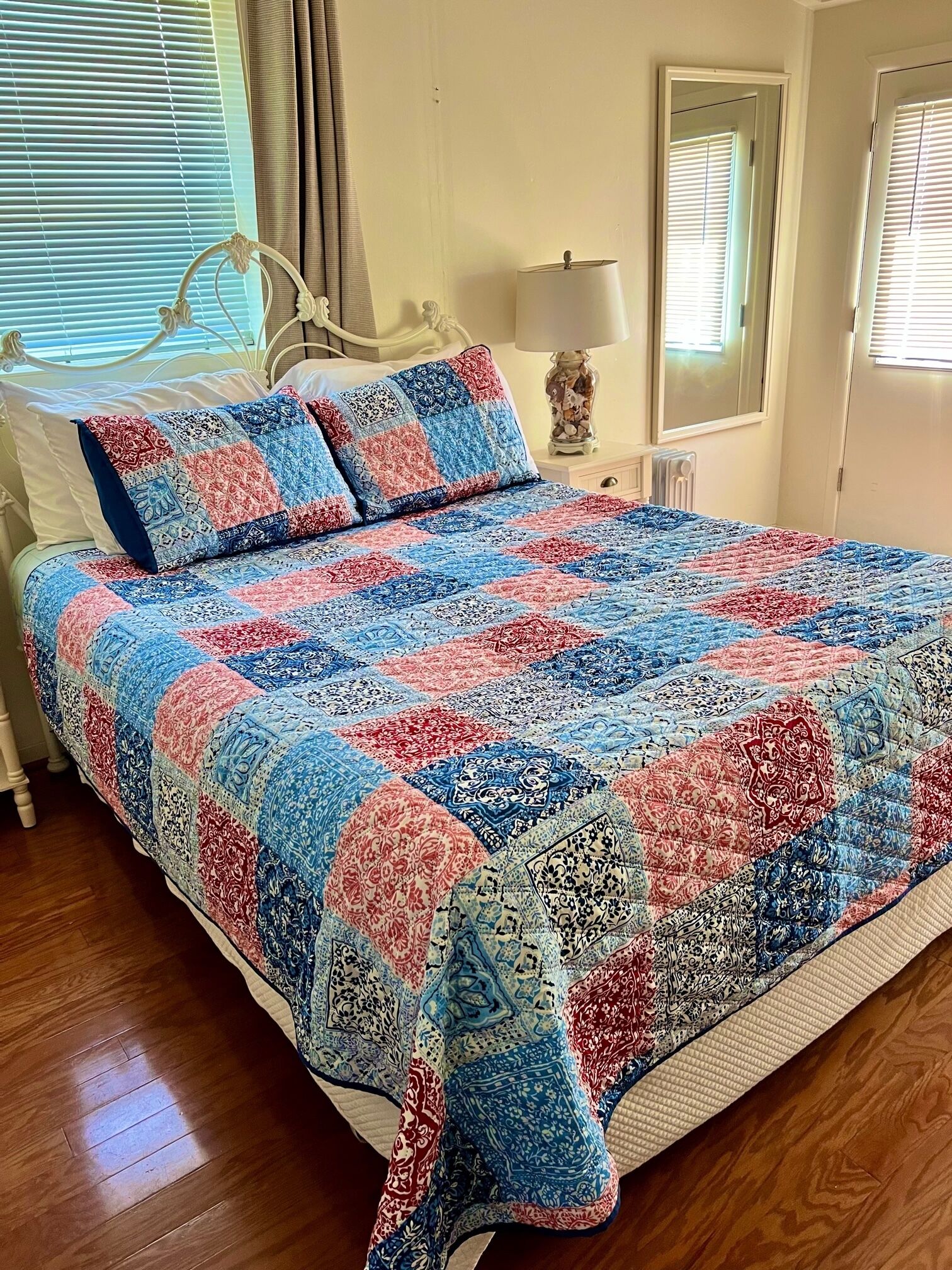 A bedroom with a bed, a nightstand, a lamp, and a window with blinds.