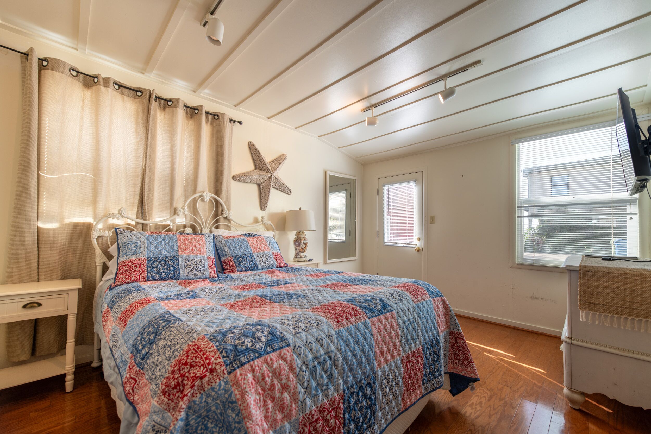 A bedroom with a large bed, a starfish decoration, a bedside table, a lamp, and a window with blinds.