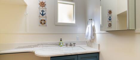 A bathroom with a white vanity, a large mirror, and nautical-themed wall decor.