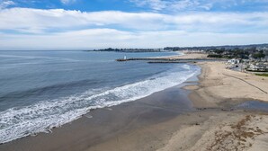 A beach with a rocky breakwater, a lighthouse, and a distant shoreline with buildings.