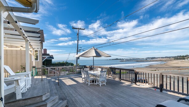 A wooden deck with a table and chairs, overlooking a beach and ocean.