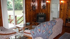 A cozy cabin interior with a wooden interior, a glass door leading to a deck, a fireplace, and a refrigerator. - The River House of Alaska, Michigan located Southeast Grand Rapids, pet friendly (Alto)