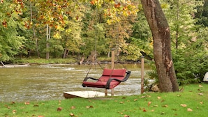 A park with a swing chair by a pond surrounded by trees. - The River House of Alaska, Michigan located Southeast Grand Rapids, pet friendly (Alto)