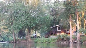 A cabin by a lake surrounded by trees. - The River House of Alaska, Michigan located Southeast Grand Rapids, pet friendly (Alto)