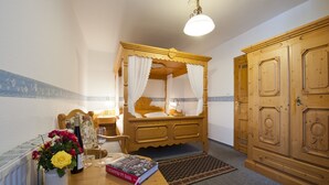 A bedroom with a wooden four-poster bed, a wooden wardrobe, a small table with a book and a vase of flowers, and a radiator on the wall. - Hotel Restaurant Zum Engel (Roemerberg)