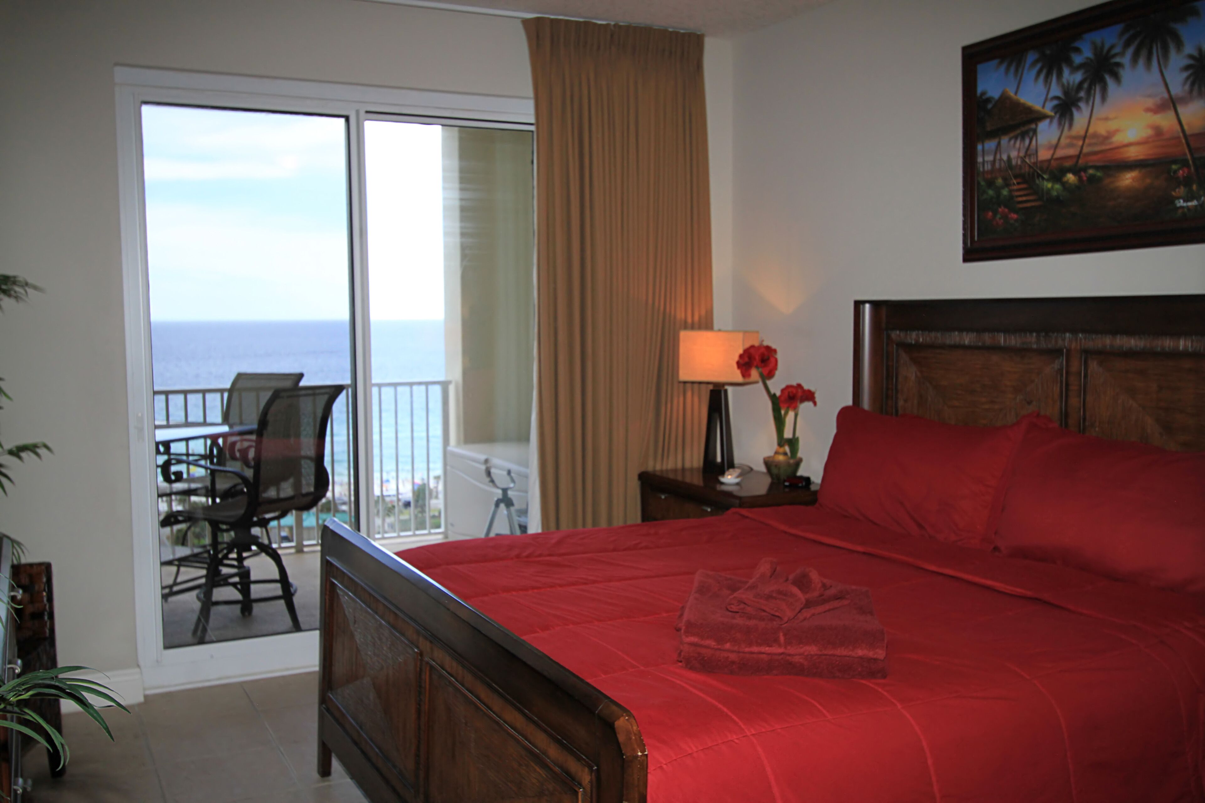 A hotel room with a large bed, a balcony with a chair, and a view of the ocean.