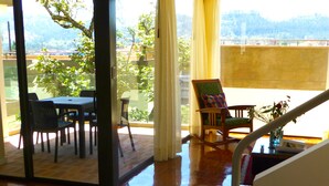 A spacious room with a sliding glass door leading to an outdoor area, a wooden table with chairs, and a rocking chair with a colorful cushion. - Riverfront condo - Amazing views in Cuenca's Historic District  (Cuenca)