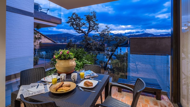 A dining area with a table set for two, a potted plant, and a view of the cityscape. - Riverfront condo - Amazing views in Cuenca's Historic District  (Cuenca)