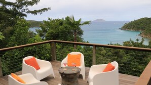 A deck with white chairs and orange cushions, overlooking a coastal landscape with trees and the sea. - Mampoo House - Luxury Vacation Rental, St. John, USVI (St. John)