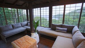 A modern living room with a sofa and a loveseat facing large windows with a view of a lush landscape. - Mampoo House - Luxury Vacation Rental, St. John, USVI (St. John)