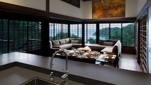 A modern kitchen with a large island, dining area with a sofa, and large windows offering a view of the outdoors. - Mampoo House - Luxury Vacation Rental, St. John, USVI (St. John)
