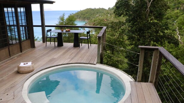 A hot tub on a wooden deck with a table and chairs, overlooking a scenic view of the ocean and hills. - Mampoo House - Luxury Vacation Rental, St. John, USVI (St. John)