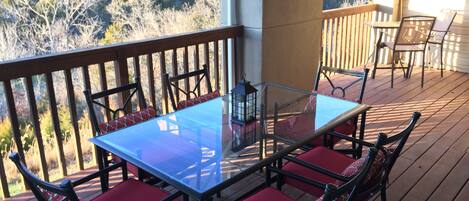Une terrasse extérieure couverte, dotée d’une table à plateau de verre et de chaises rembourrées rouges, qui offre une vue sur une zone boisée.