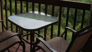 A wooden deck with a glass table and two chairs, overlooking a forested valley and a lake. - This Is Our Completely Remodeled Place On The Lake! Right Next To Sdc! (Branson)