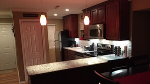 A kitchen with granite countertops, wooden cabinets, a stainless steel refrigerator, a microwave, and a stove. There are two pendant lights and a red cloth on the table. - This Is Our Completely Remodeled Place On The Lake! Right Next To Sdc! (Branson)