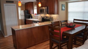 A kitchen with wooden cabinets, a granite countertop, a stainless steel refrigerator, a microwave, and a dining area with wooden chairs and a red placemat. - This Is Our Completely Remodeled Place On The Lake! Right Next To Sdc! (Branson)