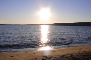 A beach with a clear sky and calm water reflecting the sun.