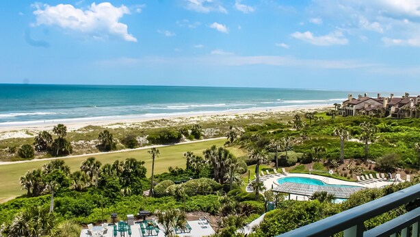 A resort with a pool, beach view, and lush greenery.