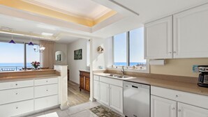 A modern kitchen with white cabinetry, a dishwasher, and a view of the sea.