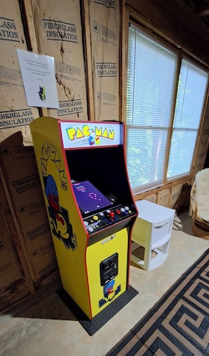 Ett Pac-Man-spel i ett arkadskåp, placerat i ett rum med träväggar och isoleringspaneler.