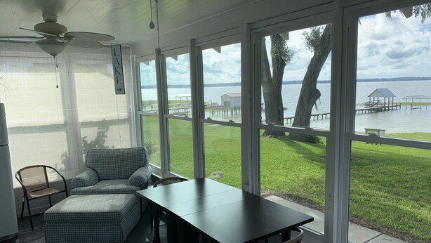 A sunroom with a view of a lake, a table, and a couch. - Lake front on North shore of Lake Weir, Florida (it is NOT a duplex / 2 entries) (Ocklawaha)