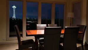A dining area with a table and chairs, large windows with a view of the Space Needle, and a lamp on the right. - Luxury in Queen Anne very walkable! (Seattle)