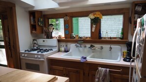 A kitchen with wooden cabinets, a stove, a sink, and a window with a view of greenery. - Classic Vermont Cabin on 2.5 acres Lake Frontage (Salisbury)