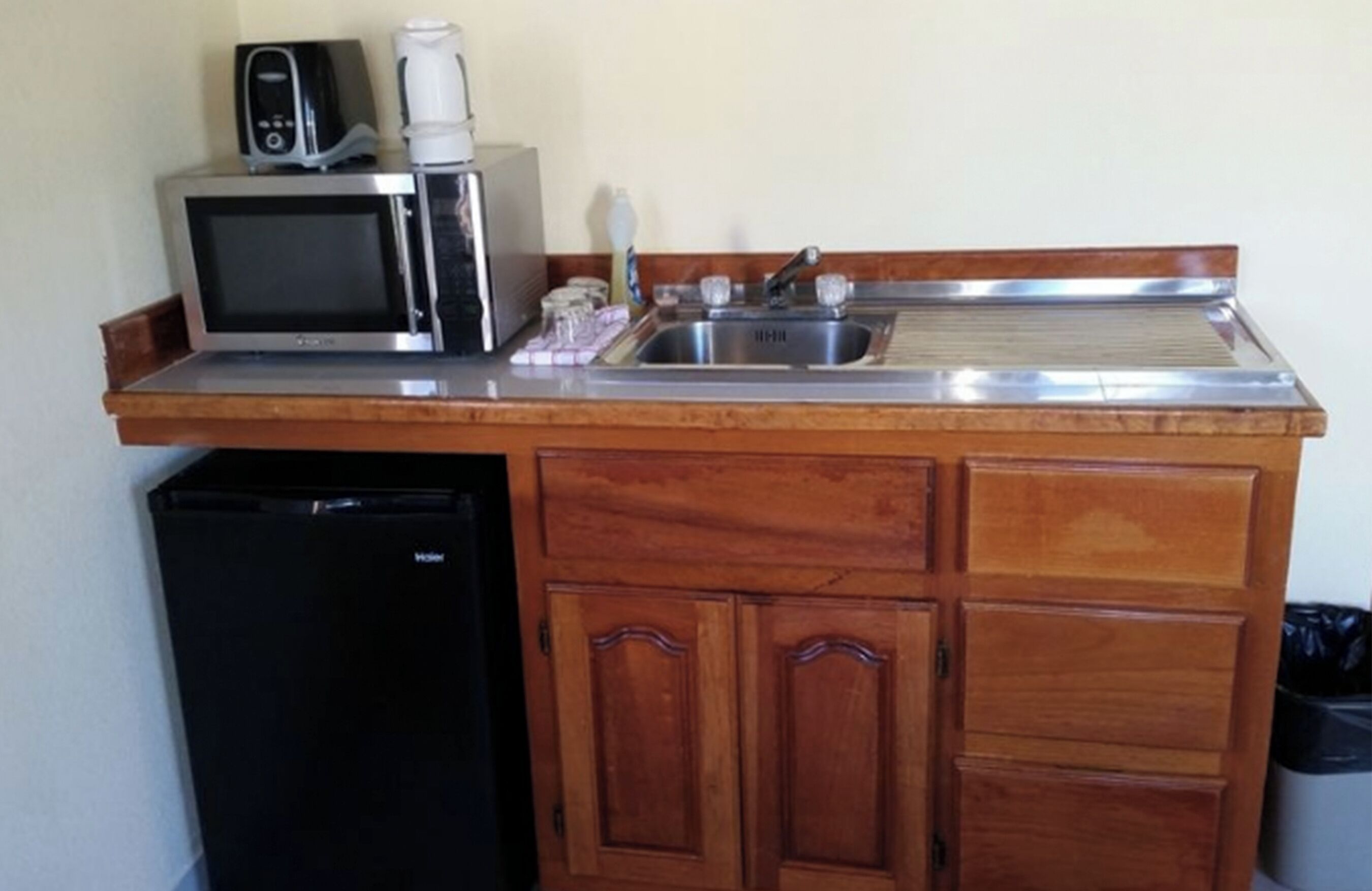 Una kitchenette compacta equipada con microondas, cafetera y lavamanos.