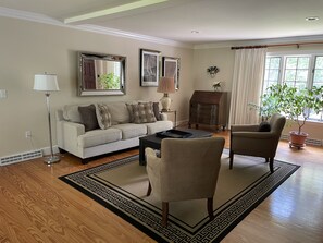 Un salon comprenant un canapé, deux fauteuils, une table basse, une cheminée et une grande fenêtre avec des rideaux.