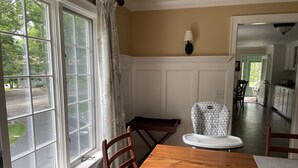 A dining area with a wooden table and chairs, a high chair, a window with curtains, and a view of the street. - Beautiful vacation home in amazing location (York)
